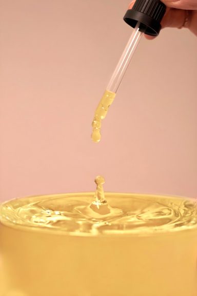 Eine Pipette tropft goldenes Öl in eine runde Schale.