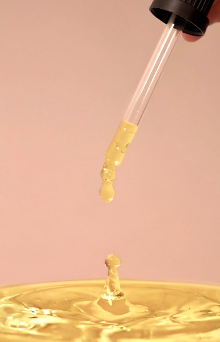 Tropfen aus einer Pipette fallen in eine goldene Flüssigkeit.
