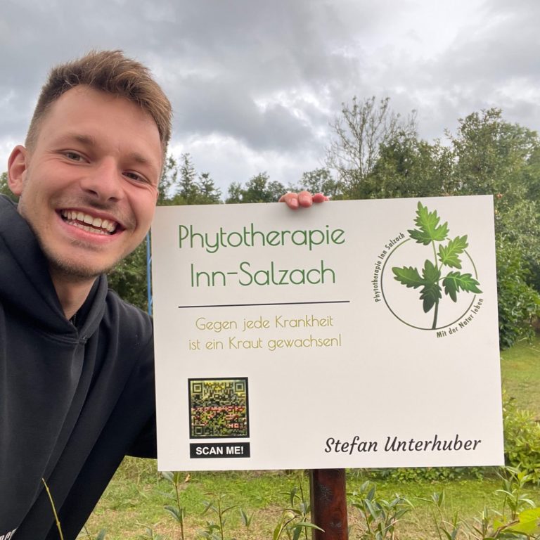 Lächelnder Mann steht neben einem Schild für die Physiotherapie Inn-Salzach.