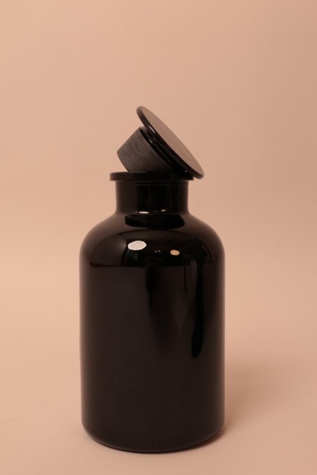 Schwarze Flasche mit schrägem Deckel vor einem neutralen Hintergrund.